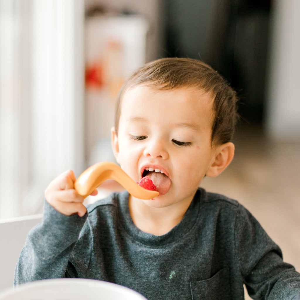 little boy using a Kizingo spoon and tasting a raspberry